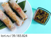 Три свежих спринг-ролла с начинкой из морепродуктов и овощей и темный соус на светло-синем фоне. Стоковое фото, фотограф Лозовая Людмила / Фотобанк Лори