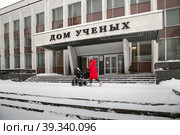 Город Обнинск, проспект Ленина, 129. Девушка в красном пальто с детской коляской идет мимо Дома ученых (МП "Дом ученых") в зимний пасмурный день (2021 год). Редакционное фото, фотограф Наталья Николаева / Фотобанк Лори