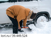 A man digs out a stalled car in the snow with a car shovel. Transport in winter got stuck in a snowdrift after a snowfall, sat on the bottom. First aid, tow truck, winter tires spikes and all-season. Стоковое фото, фотограф Ольга Симонова / Фотобанк Лори