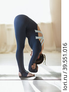 A woman leading a healthy lifestyle, exercising in sportswear, performs forward bends to stretch the muscles of the back and legs, standing on a mat in the room. Стоковое фото, фотограф Сергей Чайко / Фотобанк Лори