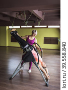 Woman trainer giving inversion therapy to student, hanging upside down on inversion table in room. Стоковое фото, фотограф Сергей Чайко / Фотобанк Лори