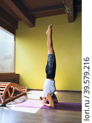 A woman performs the sirshasana exercise, an inverted asana, stands on a mat in the studio. Стоковое фото, фотограф Сергей Чайко / Фотобанк Лори