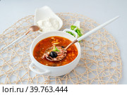 Мясная Солянка. сборная солянка. порция острого красного мясного супа с помидорами, копченостями сосисками и оливками с лимоном на светлом фоне. Стоковое фото, фотограф Оксана Медведева / Фотобанк Лори