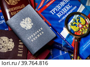 Паспорт, военный билет и трудовая книжка сотрудника, Трудовой кодекс Российской Федерации лежат на столе в отделе кадров предприятия (2023 год). Редакционное фото, фотограф Николай Винокуров / Фотобанк Лори