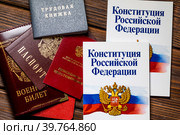 Паспорт, военный билет, трудовая книжка сотрудника, пенсионное удостоверение и Конституция Российской Федерации лежат на столе в отделе кадров предприятия (2023 год). Редакционное фото, фотограф Николай Винокуров / Фотобанк Лори
