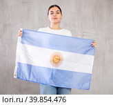 Joyous young woman holding Argentina flag against unicoloured background. Стоковое фото, фотограф Яков Филимонов / Фотобанк Лори