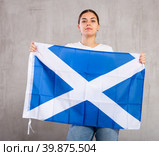 Serious young woman waving state flag of Scotland against gray wall background. Стоковое фото, фотограф Яков Филимонов / Фотобанк Лори