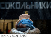 Девушка идет по улице укутавшись в шарфы к метро "Сокольники" в холодную промозглую погоду в городе Москве, Россия (2023 год). Редакционное фото, фотограф Николай Винокуров / Фотобанк Лори