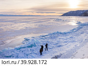 Baikal Lake in winter at sunset. Group of tourists inspects the high ice heaps and blue icy hummocks higher than human growth formed along the coast due to the earthquake. Winter ice travel and outdoors. Стоковое фото, фотограф Виктория Катьянова / Фотобанк Лори