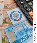 Калькулятор, конверт с эмблемой Федеральной налоговой службы и российские деньги (2023 год). Редакционное фото, фотограф Цибаев Алексей / Фотобанк Лори