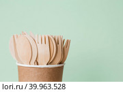 Экологически чистая одноразовая кухонная утварь в бумажном стаканчике на бежево-зеленом фоне. Деревянные вилки, ложки и ножи. Экология, концепция нулевых отходов. Стоковое фото, фотограф Photojuli / Фотобанк Лори