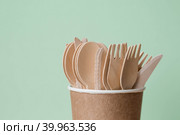 Экологически чистая одноразовая кухонная утварь в бумажном стаканчике на бежево-зеленом фоне. Деревянные вилки, ложки и ножи. Экология, концепция нулевых отходов. Стоковое фото, фотограф Photojuli / Фотобанк Лори