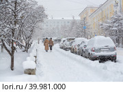 Заснеженная городская улица во время сильного снегопада. Много снега на тротуаре, машинах и ветках деревьев. Женщины гуляют по зимнему городу. Холодная снежная погода. Магадан, Сибирь, Дальний Восток России. Стоковое фото, фотограф Андрей Степанов / Фотобанк Лори