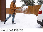 A man in winter cleans snow with a shovel in the yard of a house in the parking lot. Snowfall, difficult weather conditions, the car is stalling, digging up the passage. Стоковое фото, фотограф Ольга Симонова / Фотобанк Лори