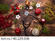Christmas flat lay on a medical theme. Decorations for the new year from stars, ball, ribbons, Santa hats, and a doctor's stethoscope. Wooden background, space for text. Стоковое фото, фотограф Ольга Симонова / Фотобанк Лори