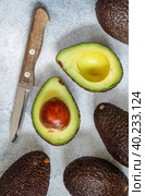 Whole and cut in half ripe organic avocados and a knife on a grey  background. The Haas Avocado. Source of vitamins , trace elements , beta-carotene and omega-3 fatty acids . Healthy food, diet. Стоковое фото, фотограф Виктория Панченко / Фотобанк Лори