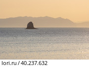 Утренний морской пейзаж. Вид на морской залив и скалу в море. Горы вдалеке. Золотистый солнечный свет на рассвете. Бухта Гертнера, Охотское море, Магаданская область, Дальний Восток России. Стоковое фото, фотограф Андрей Степанов / Фотобанк Лори
