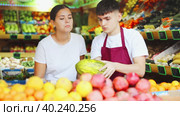 Friendly guy seller helps a girl buyer who came to the store for shopping, choose a melon. Стоковое видео, видеограф Яков Филимонов / Фотобанк Лори