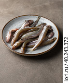 Small raw fish, snetok or smelt on a plate. Close-up, vertical view. Стоковое фото, фотограф Bogdanova Mariia / Фотобанк Лори