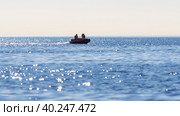 Моторная резиновая лодка плывет по морю. В лодке мужчина и женщина. Яркие солнечные блики на поверхности воды. Размытый передний план. Охотское море, Магаданская область, Россия. Стоковое фото, фотограф Андрей Степанов / Фотобанк Лори