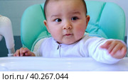 A hungry baby taps his hand on the table on a high chair, asks to eat, nibbles on a spoon. Teething, whims, itchy gums, introduction of complementary foods. Стоковое видео, видеограф Ольга Симонова / Фотобанк Лори
