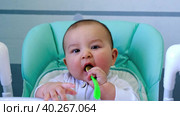 A hungry baby is gnawing on a plastic spoon at the table on a high chair. Teething, whims, itchy gums, introduction of complementary foods. Стоковое видео, видеограф Ольга Симонова / Фотобанк Лори