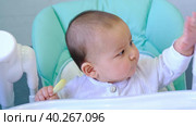 A hungry baby is gnawing on a plastic spoon at the table on a high chair. Teething, whims, itchy gums, introduction of complementary foods. Стоковое видео, видеограф Ольга Симонова / Фотобанк Лори