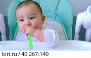 A hungry baby is gnawing on a plastic spoon at the table on a high chair. Teething, whims, itchy gums, introduction of complementary foods. Стоковое видео, видеограф Ольга Симонова / Фотобанк Лори