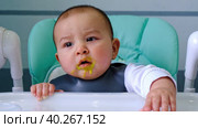 A hungry baby taps his hand on the table on a high chair, asks to eat, nibbles on a spoon. Teething, whims, itchy gums, introduction of complementary foods. Стоковое видео, видеограф Ольга Симонова / Фотобанк Лори