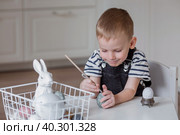 A little boy paints eggs on Maundy Thursday for the holiday. We are preparing the family for a Bright Easter. In the hands of a child, a brush and an egg. Стоковое фото, фотограф Photojuli / Фотобанк Лори
