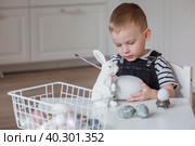 A little boy and a white Easter bunny. We are preparing the family for a Bright Easter. A child is playing with eggs. Стоковое фото, фотограф Photojuli / Фотобанк Лори