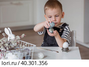 A little boy holds Easter eggs in his hands and hits them against each other. Easter is a bright holiday. A child is playing with eggs. Стоковое фото, фотограф Photojuli / Фотобанк Лори
