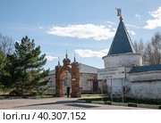 Можайский Лужецкий Ферапонтов мужской монастырь. Мужчина фотографирует монастырь, стоя в арке ворот хозяйственного двора. Дорожный указатель с надписью: "Святой колодец преподобного Ферапонта  в д. Исавиць от года 1408" (2022 год). Редакционное фото, фотограф Наталья Николаева / Фотобанк Лори