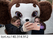 Девушки делают селфи с ростовая фигурой Чебурашки на улице Петровка в центре города Москвы, Россия (2023 год). Редакционное фото, фотограф Николай Винокуров / Фотобанк Лори