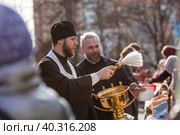 Russia, the City of Vidnoye, April 15, 2023. Easter service. The priest sprinkles people and Easter treats with holy water at the entrance to the temple. People go to sanctify eggs and cakes. Редакционное фото, фотограф Photojuli / Фотобанк Лори