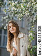 A beautiful girl in a long beige raincoat basks in the sun 2977. Стоковое фото, фотограф Алёна Замотаева / Фотобанк Лори