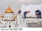 A team of workers lay tiles and repair asphalt against the background of the Cathedral of Christ the Savior in Moscow. Construction works in the city. (2023 год). Редакционное фото, фотограф Photojuli / Фотобанк Лори