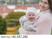 A young mother holds a charming little son in her arms. The kid looks at the camera and smiles. Portrait of a beautiful chubby 4-month-old baby. Стоковое фото, фотограф Photojuli / Фотобанк Лори