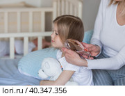 A happy young mother combs her adorable little daughter's hair while sitting in bed in the morning. The girl smiles. Family and care. Стоковое фото, фотограф Photojuli / Фотобанк Лори