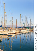 Greece. Crete. Beautiful seascape with yachts in marina of Agios Nikolaos in setting sun. The masts of the yachts are reflected in the blue water of the Mirabello Bay. Summer travel and seaside holidays (2014 год). Стоковое фото, фотограф Виктория Катьянова / Фотобанк Лори
