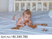 A charming boy in a bright bedroom. A newborn baby is lying on the bed and gnawing on toys. Teeth are teething. The baby's gums are itching. Family, pregnancy and childbirth. Стоковое фото, фотограф Photojuli / Фотобанк Лори
