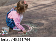 A happy girl in pink clothes draws a rainbow with chalk on the asphalt on the street. Portrait of a little girl drawing with rainbow chalk on a sunny summer day. Creative development of children. Стоковое фото, фотограф Photojuli / Фотобанк Лори