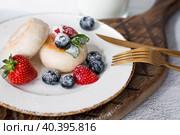 Cottage cheese pancakes, Russian cheesecakes with fresh blueberries, strawberries and mint on a stylish wooden board on a gray concrete table. Natural products. Healthy and delicious breakfast. Стоковое фото, фотограф Photojuli / Фотобанк Лори