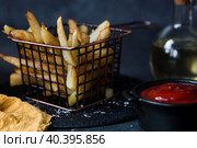 French fries in a metal basket with salt, ketchup and sunflower oil on a stylish board on a dark background. Fried potatoes. The concept of fast food and junk food. Стоковое фото, фотограф Photojuli / Фотобанк Лори