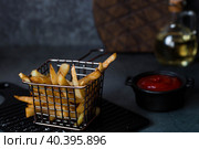 French fries in a metal basket with salt, ketchup and sunflower oil on a stylish board on a dark background. Fried potatoes. The concept of fast food and junk food. Стоковое фото, фотограф Photojuli / Фотобанк Лори
