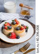 Cottage cheese pancakes, Russian cheesecakes with fresh blueberries, strawberries, honey and mint leaves on a stylish wooden board on a gray concrete table. Natural products. Healthy and delicious breakfast. Стоковое фото, фотограф Photojuli / Фотобанк Лори