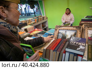 Женщина в пилотке выбирает старые книги в продаже на ретро-маркете в рамках фестиваля "Московская весна" на Никитском бульваре в центре города Москвы, Россия (2023 год). Редакционное фото, фотограф Николай Винокуров / Фотобанк Лори