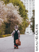 A little boy of 4 years old outdoors with a suitcase and a stuffed rabbit goes on a journey. A beautiful portrait of a child playing on the street. Стоковое фото, фотограф Photojuli / Фотобанк Лори