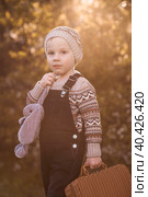 A little boy of 4 years old outdoors with a suitcase and a stuffed rabbit goes on a journey. A beautiful portrait of a child playing on the street. Стоковое фото, фотограф Photojuli / Фотобанк Лори