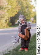 A little boy of 4 years old outdoors with a suitcase and a stuffed rabbit goes on a journey. A beautiful portrait of a child playing on the street. Стоковое фото, фотограф Photojuli / Фотобанк Лори